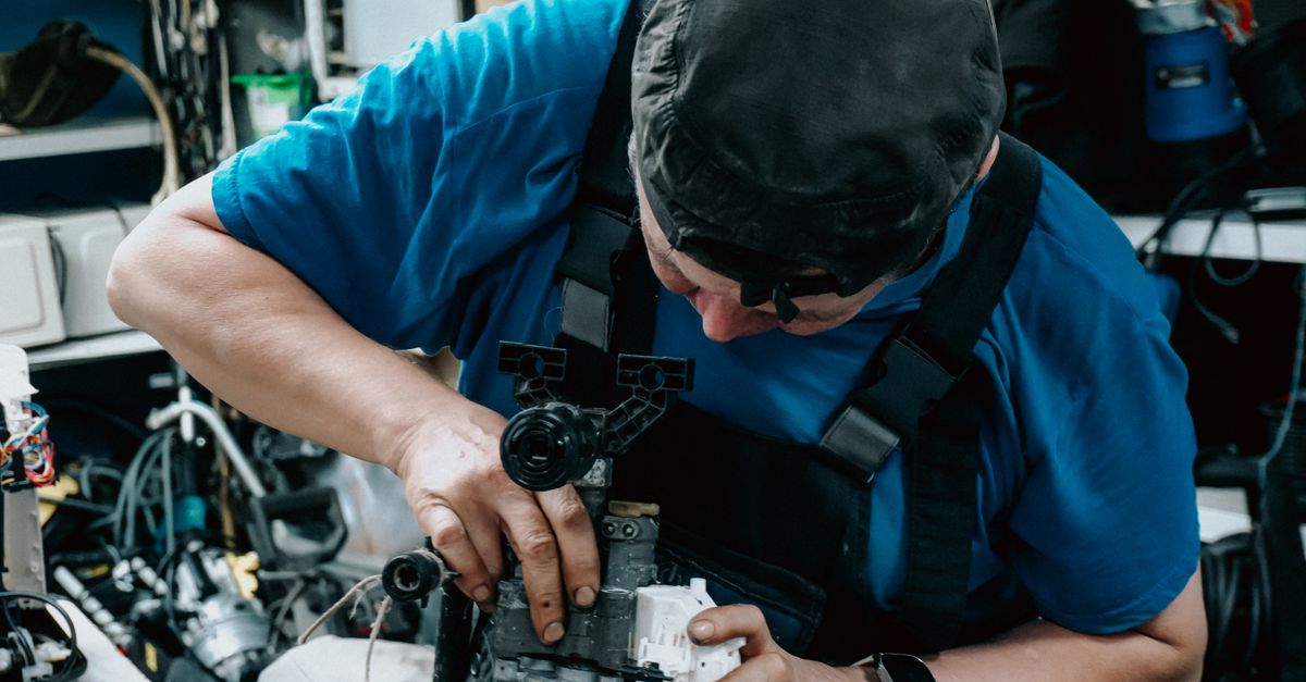 Focused technician working on machinery in a cluttered workshop, showcasing skilled labor.