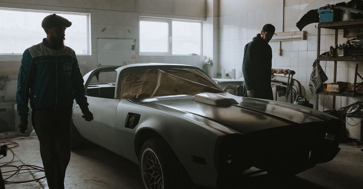 Mechanics working on a vintage car restoration in a dimly lit garage, capturing the essence of classic automotive care.