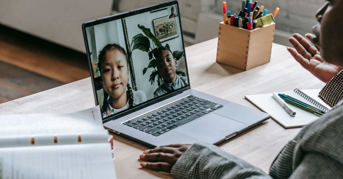 From above of crop confident African American female teacher sitting in classroom and teaching multiethnic pupils remotely on laptop during coronavirus pandemic