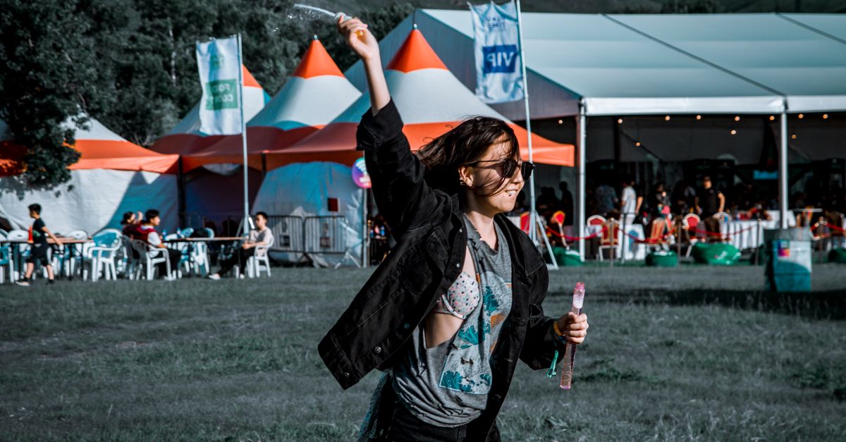 A woman joyfully plays with bubbles at an outdoor festival.